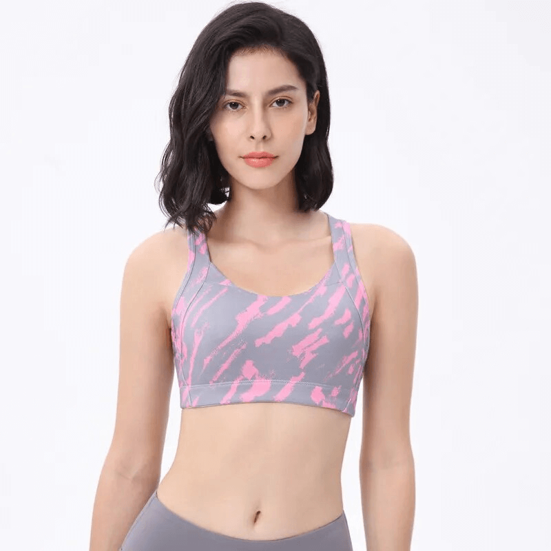 Woman wearing a stylish elastic sports bra with cross back in pink and gray for comfortable workouts.